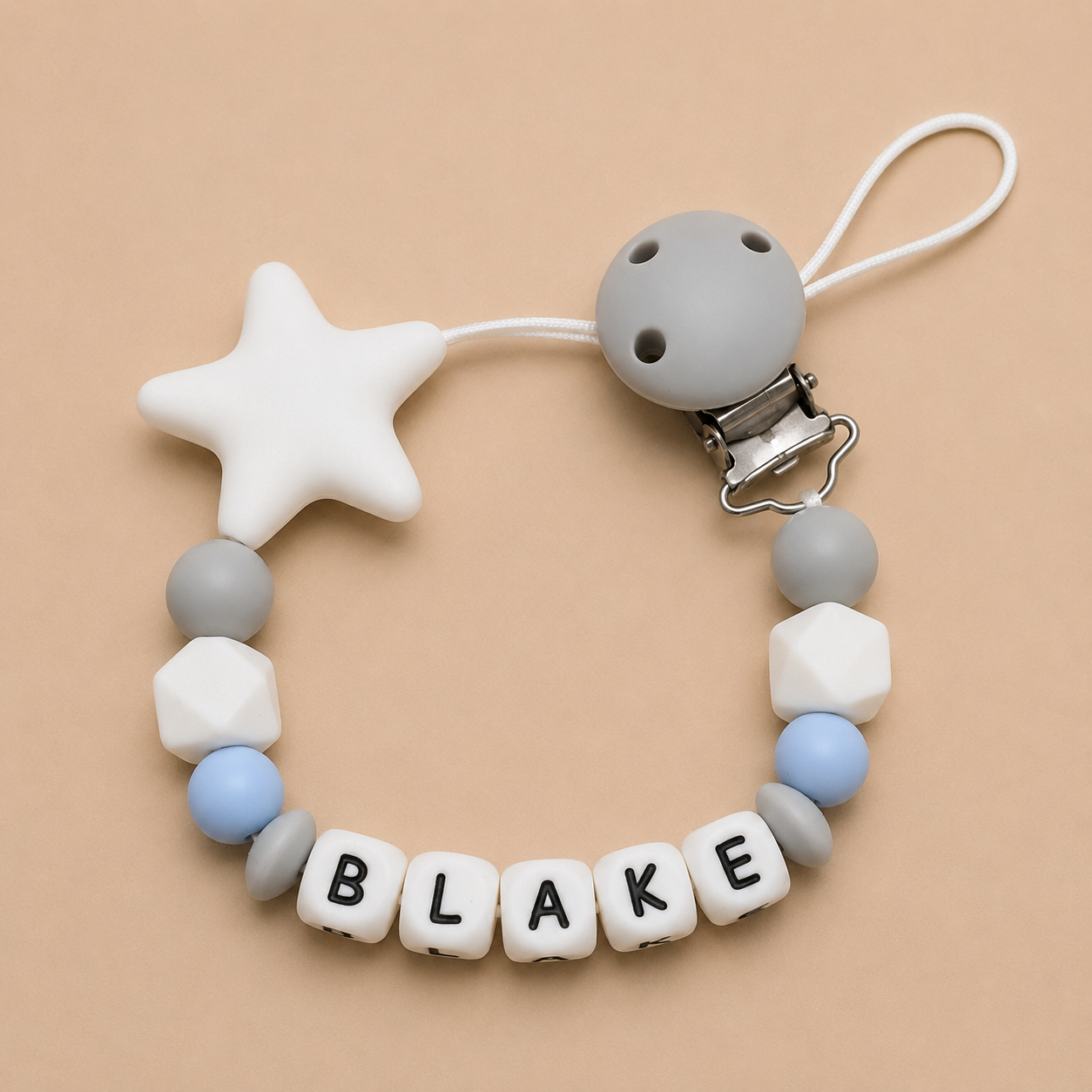 Teething ring with star-shaped bead and letter beads spelling 'BLAKE' on a beige background