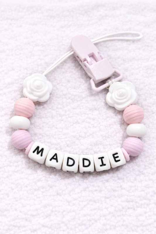 Baby teething pacifier clip with 'MADDIE' on a soft pink background