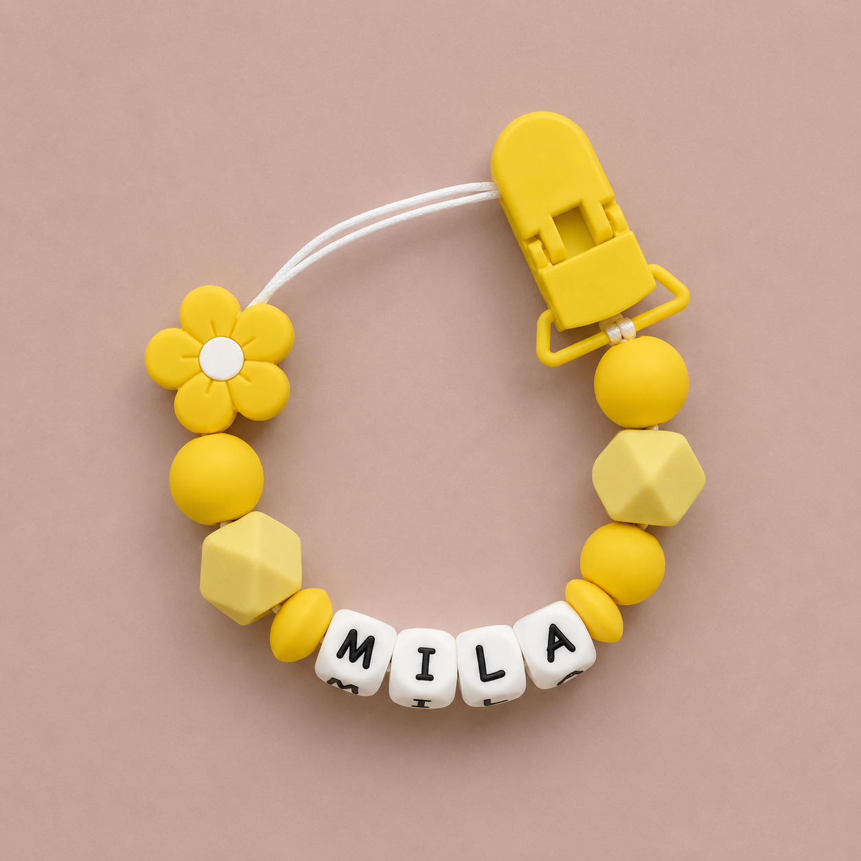 Yellow baby dummy clip with 'MILA' on a beige background