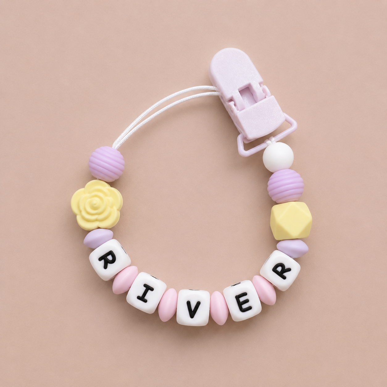 Pastel-colored pacifier clip with letter beads spelling 'RIVER' on a beige background