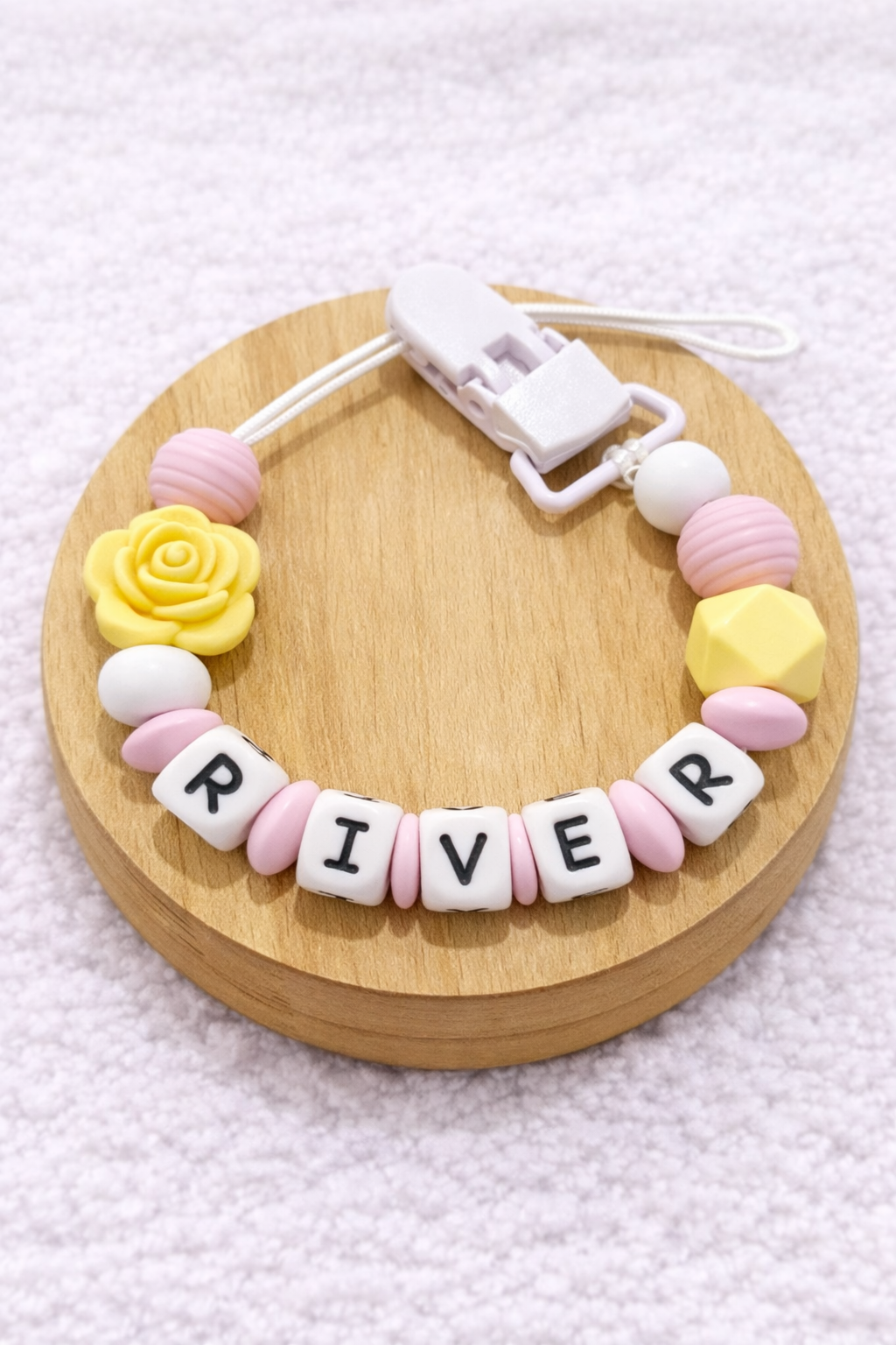pacifier clip with 'RIVER' beads on a wooden base