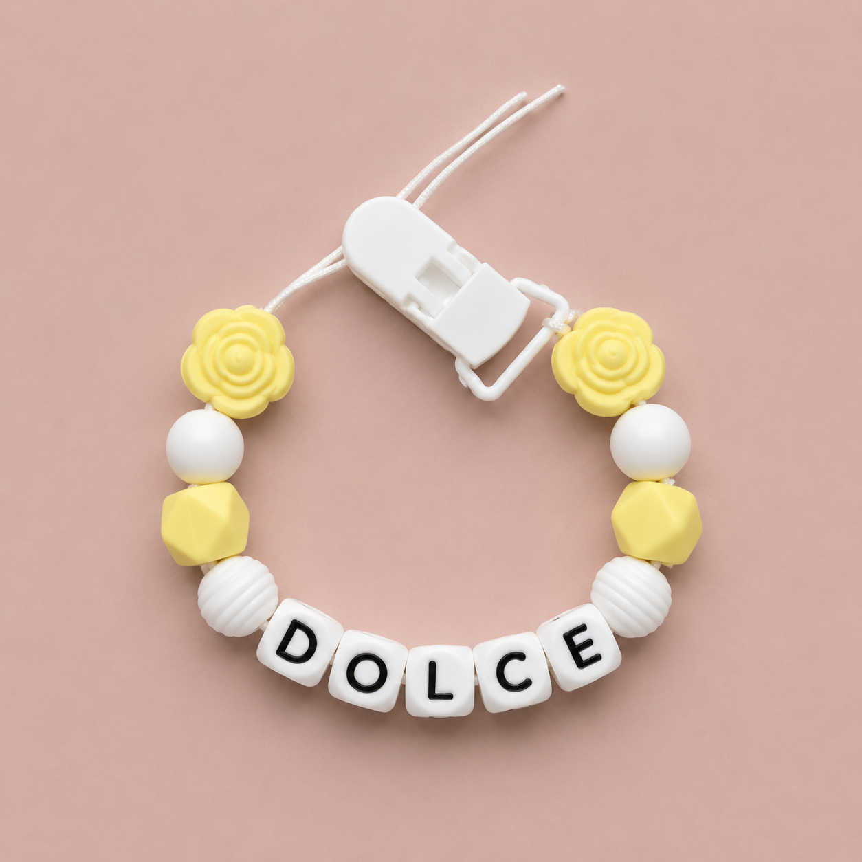 Baby dummy clip with yellow and white beads and 'DOLCE' letters on a pink background
