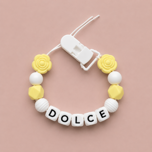 Baby dummy clip with yellow and white beads and 'DOLCE' letters on a pink background