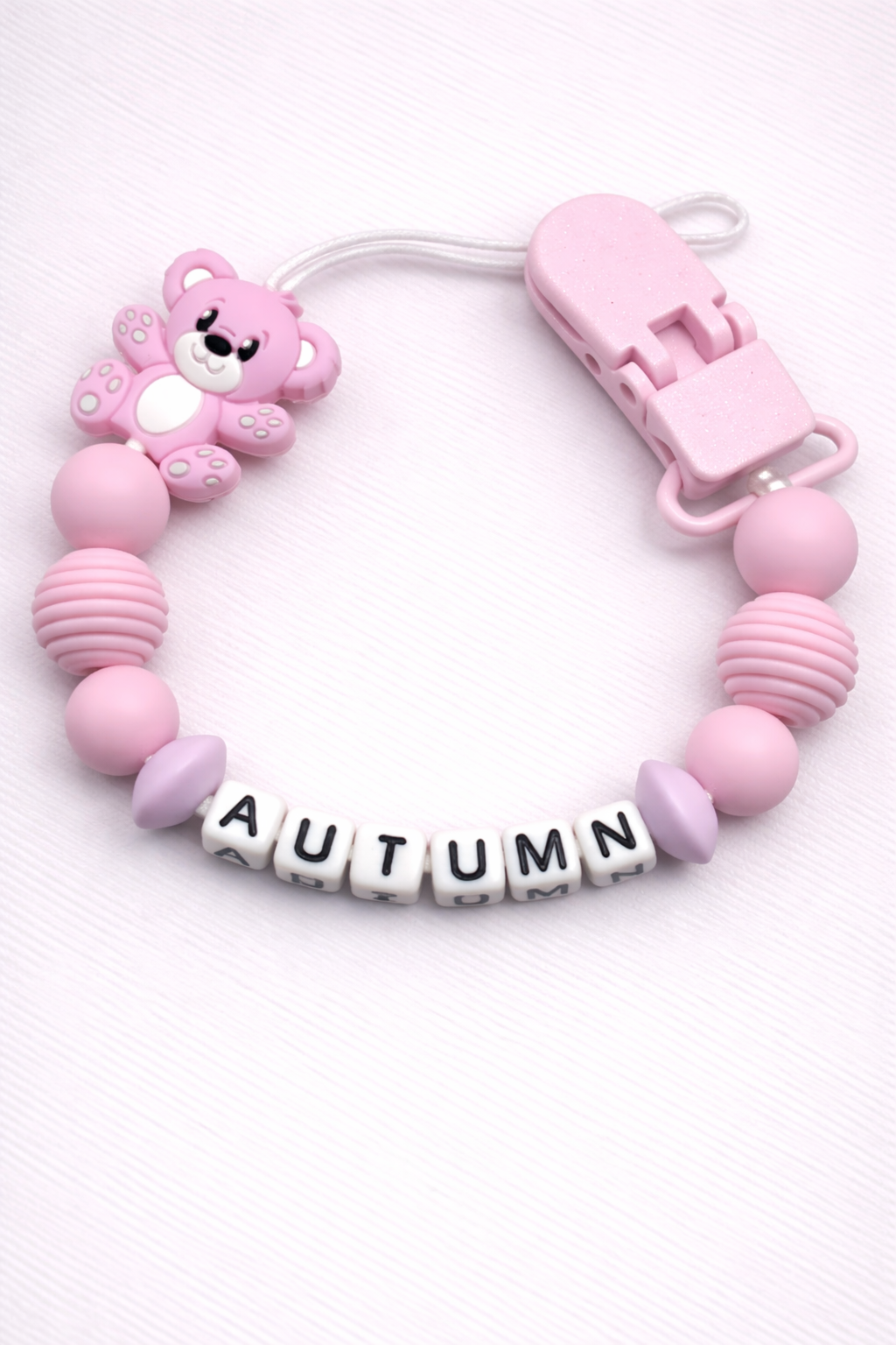 Pink baby dummy clip with letter beads spelling 'AUTUMN' on a white background