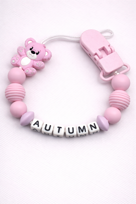 Pink baby dummy clip with letter beads spelling 'AUTUMN' on a white background