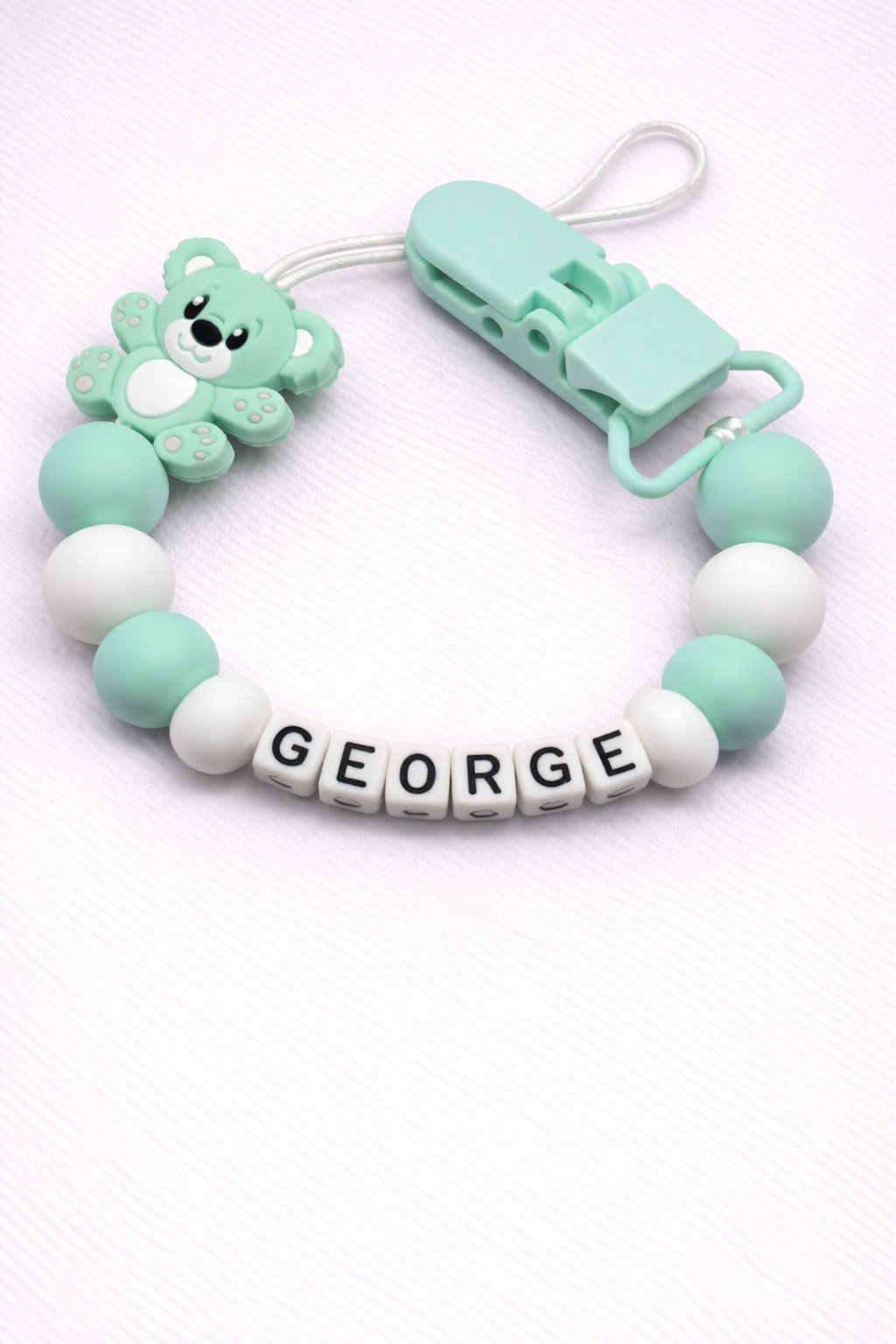 Dummy Clip with teddy bear charm and 'GEORGE' beads on a white background