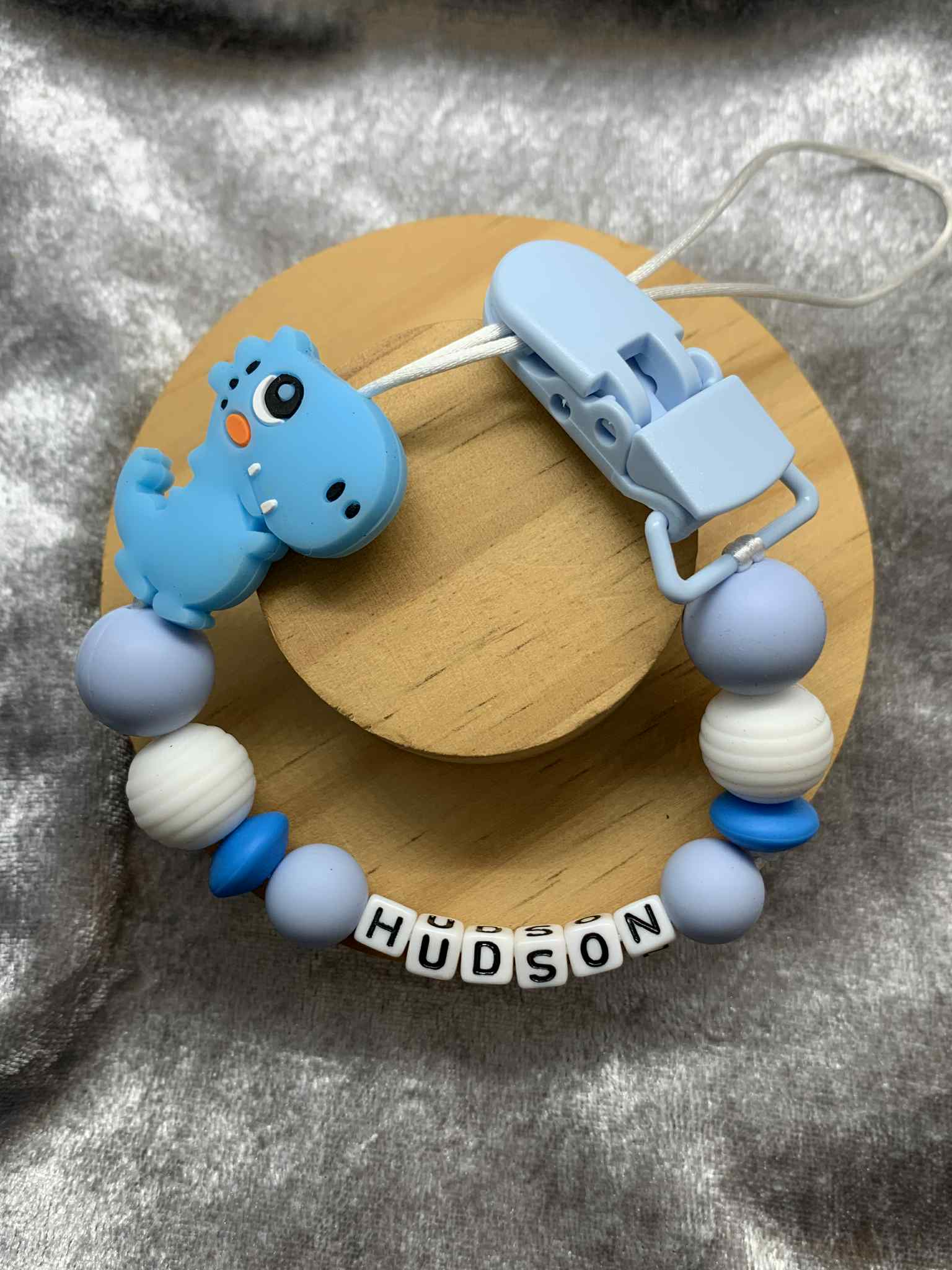 Blue personalised dummy clip featuring a dinosaur design for babies.