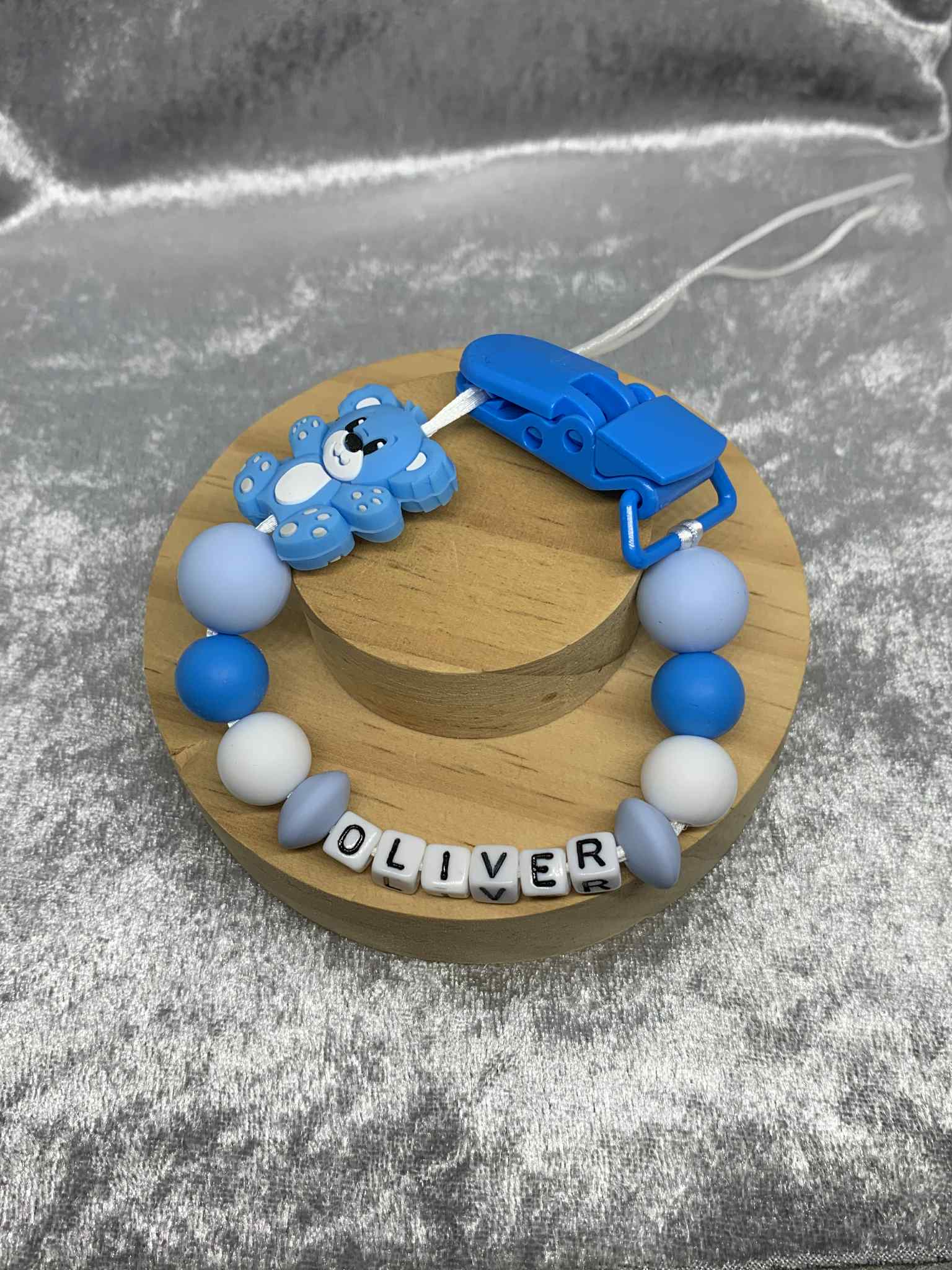 Blue and white dummy clip with a wooden base on a gray surface. Personalised.