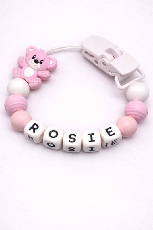 Pink and white baby teether with 'ROSIE' letters and a teddy bear charm on a white background