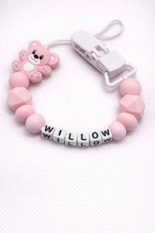 Pink dummy clip with a teddy bear charm and 'WILLOW' letter beads on a white background