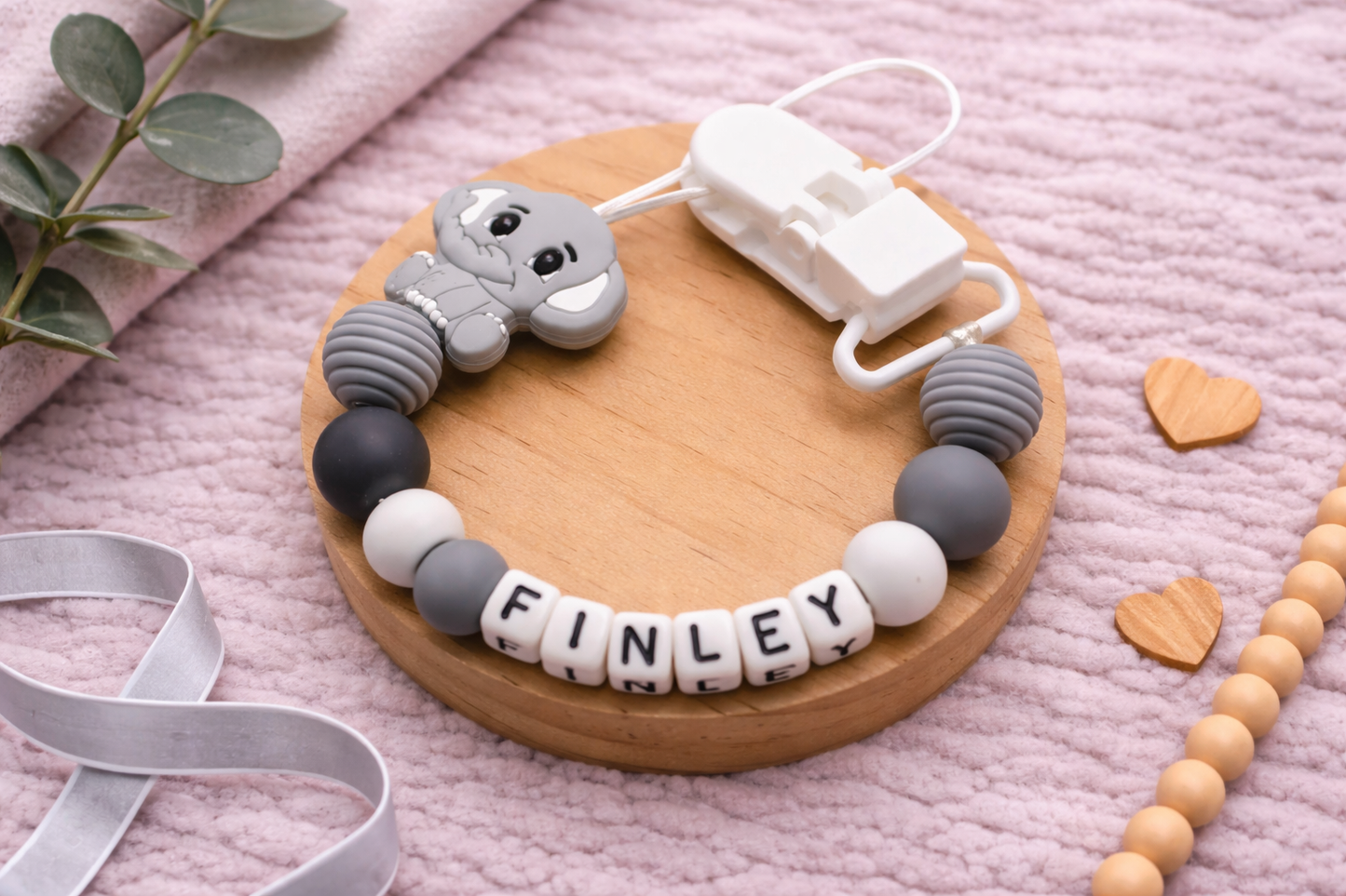  Personalized Dummy Clip with Plastic Letters with 'FINLEY' on a wooden board on a pink textured surface