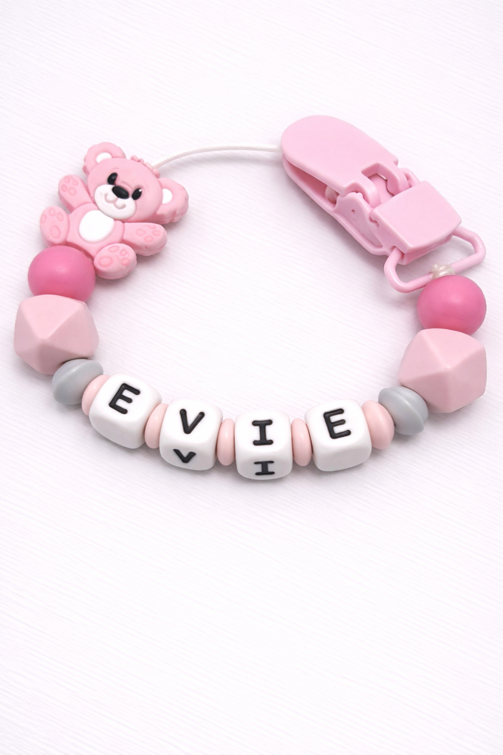 Pink and gray dummy clip with a teddy bear charm and letter beads on a white background