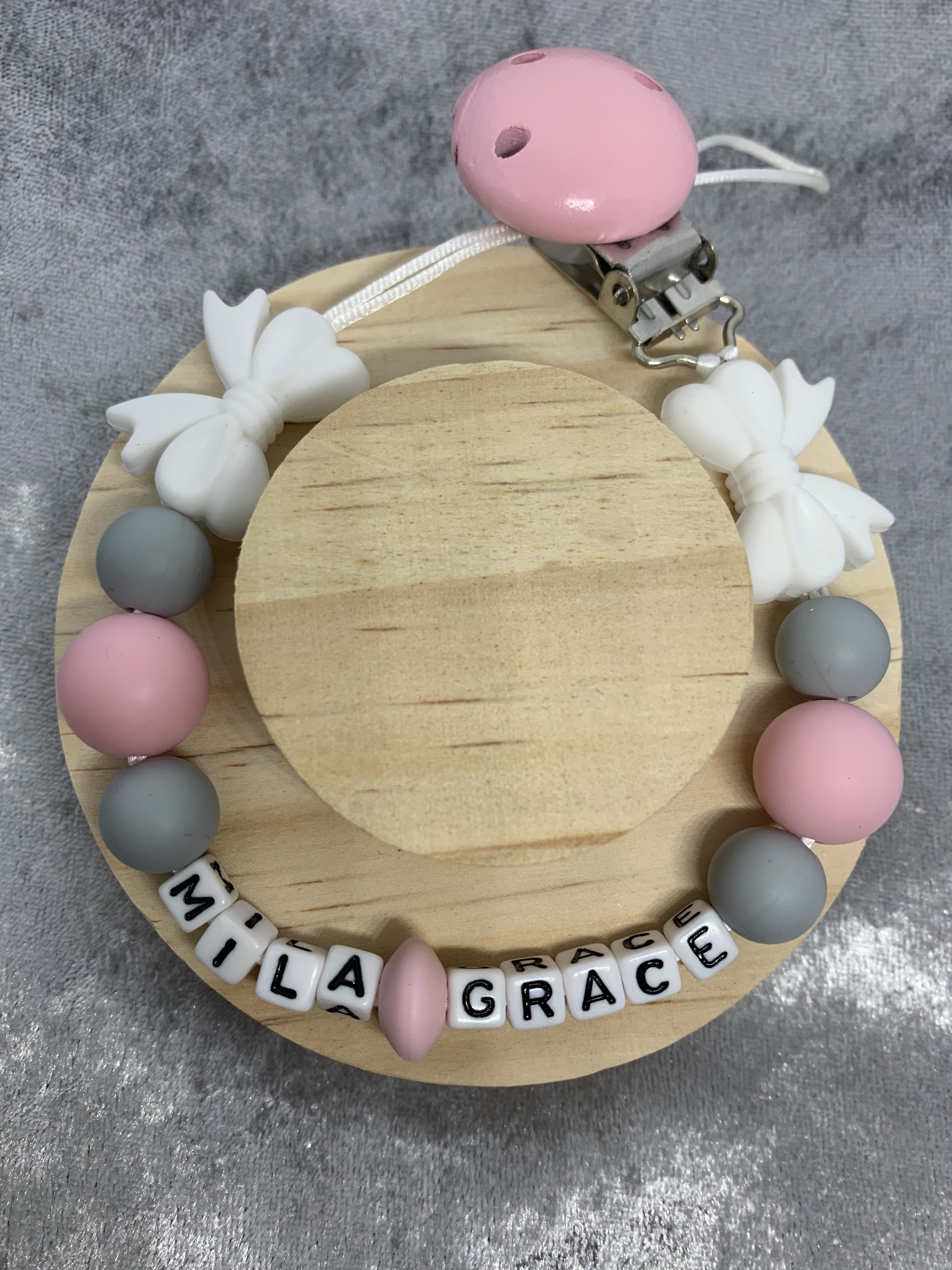 Baby teether with pink, gray, and white beads and 'Mila Grace' name on a wooden base.