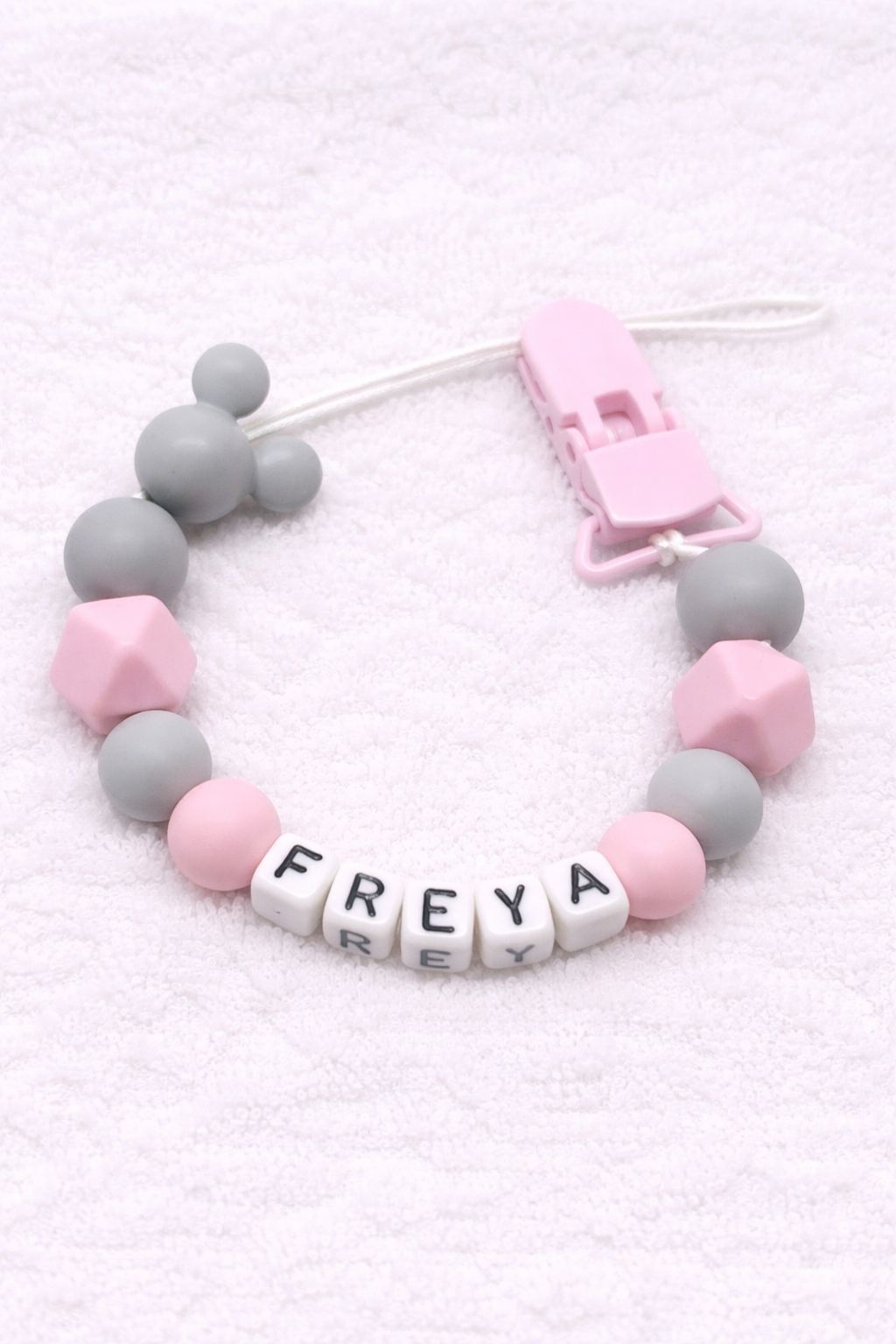 Baby dummy clip with pink and gray beads and 'FREYA' letters on a white background