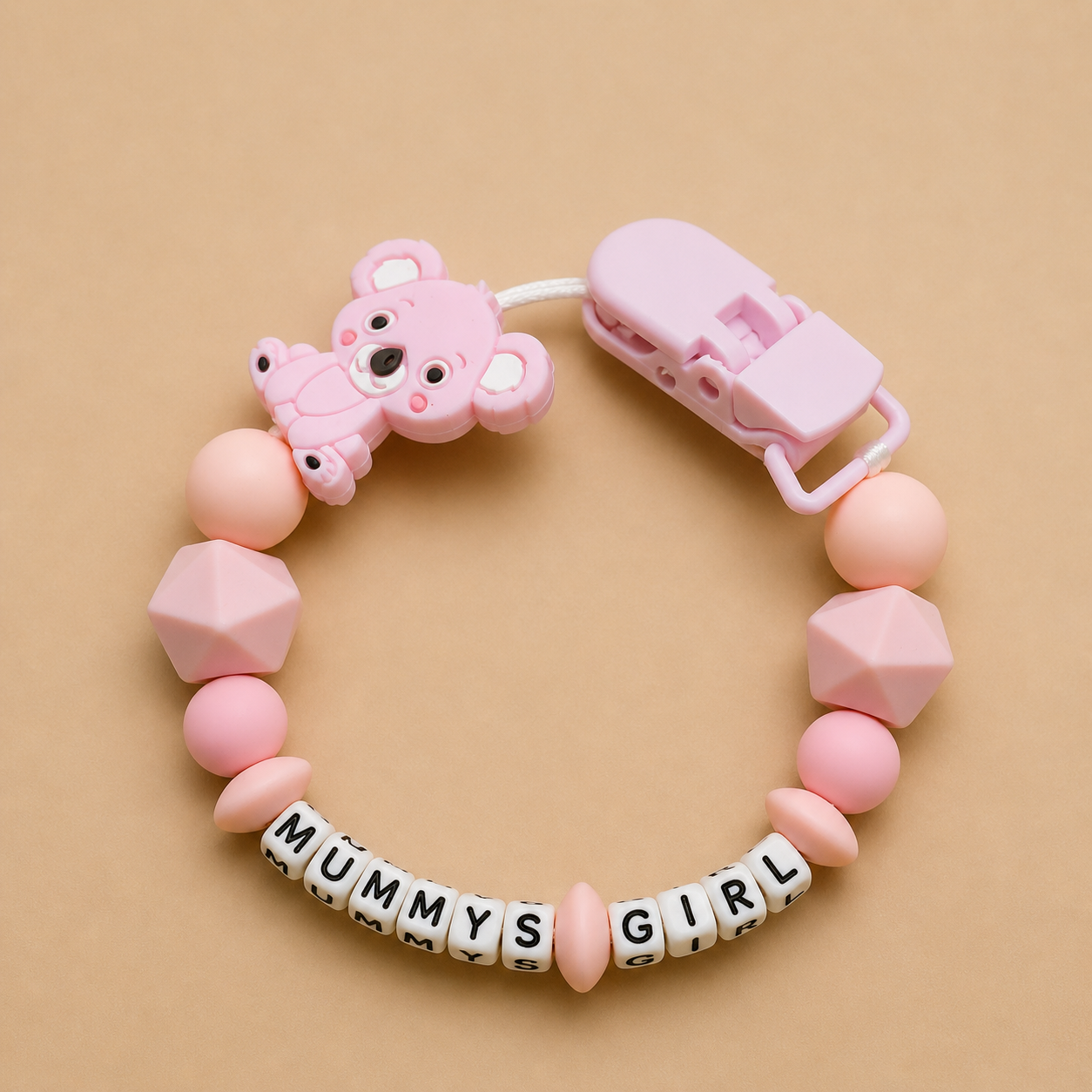 Pink baby teether with 'MUMMY'S GIRL' beads on a beige background