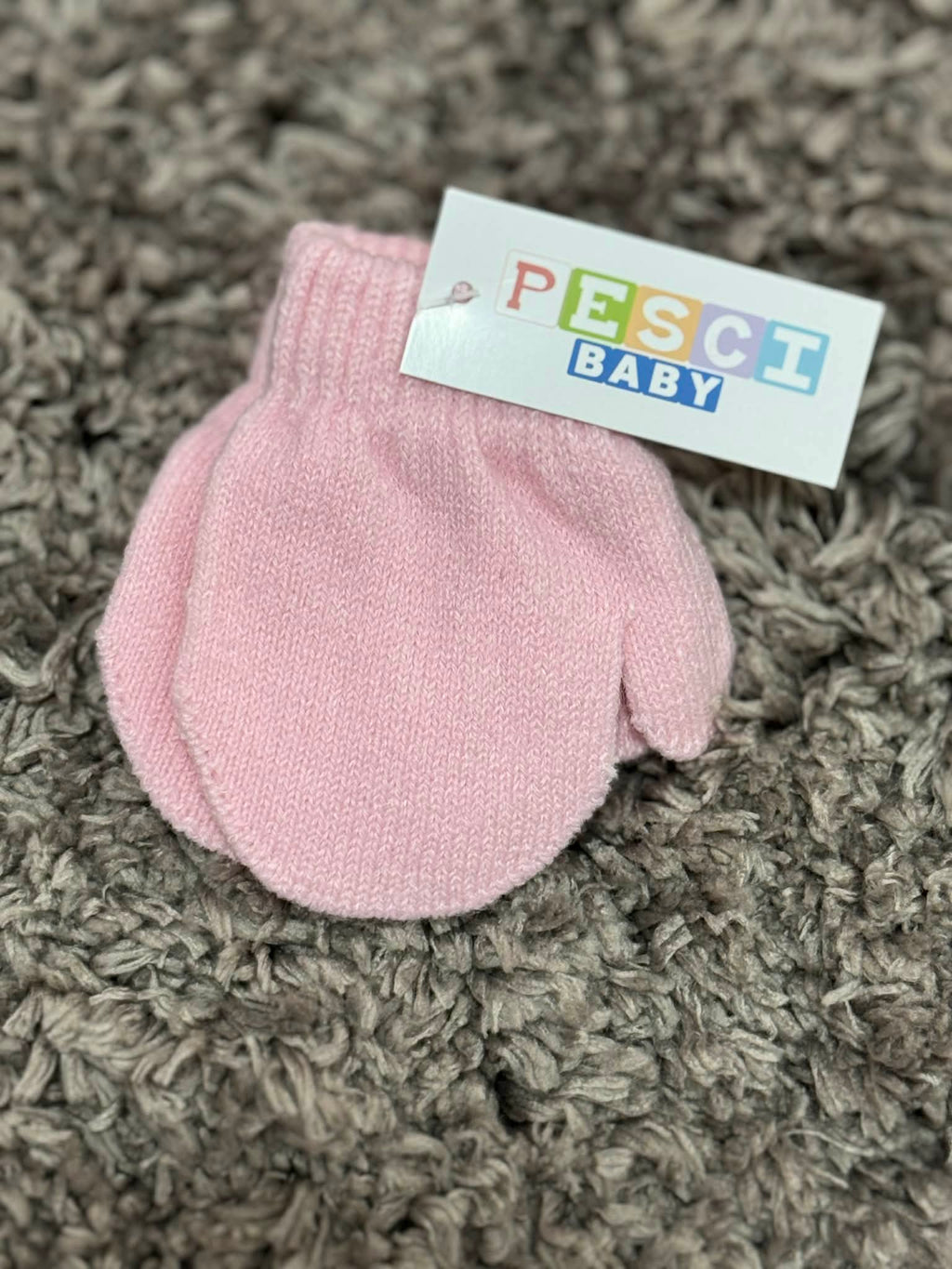 Pink baby mittens with a 'Pesci Baby' label on a textured brown surface