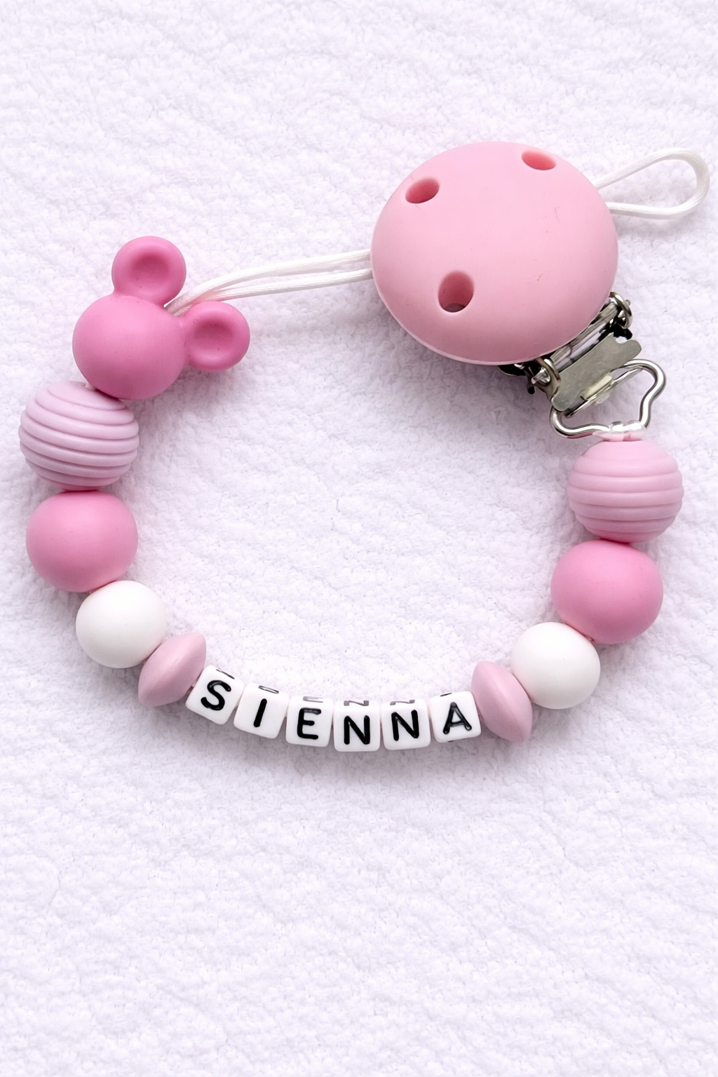Pink and white beaded pacifier clip with 'SIENNA' on a white background