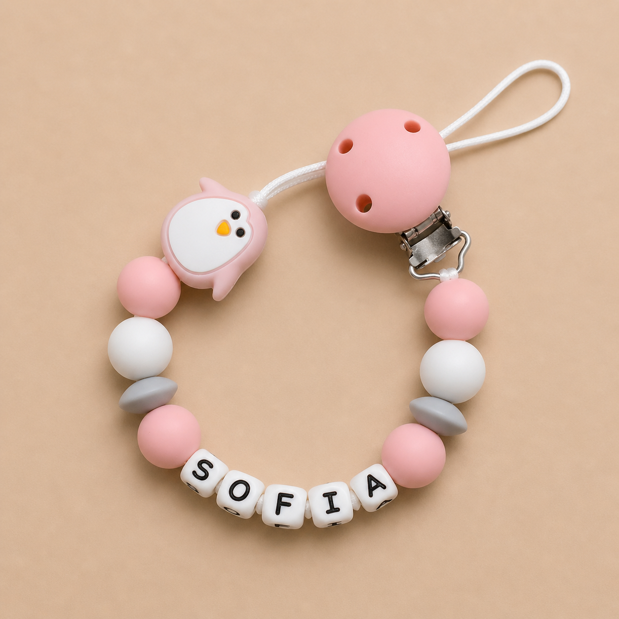 Pink and white pacifier clip with 'SOFIA' on a beige background