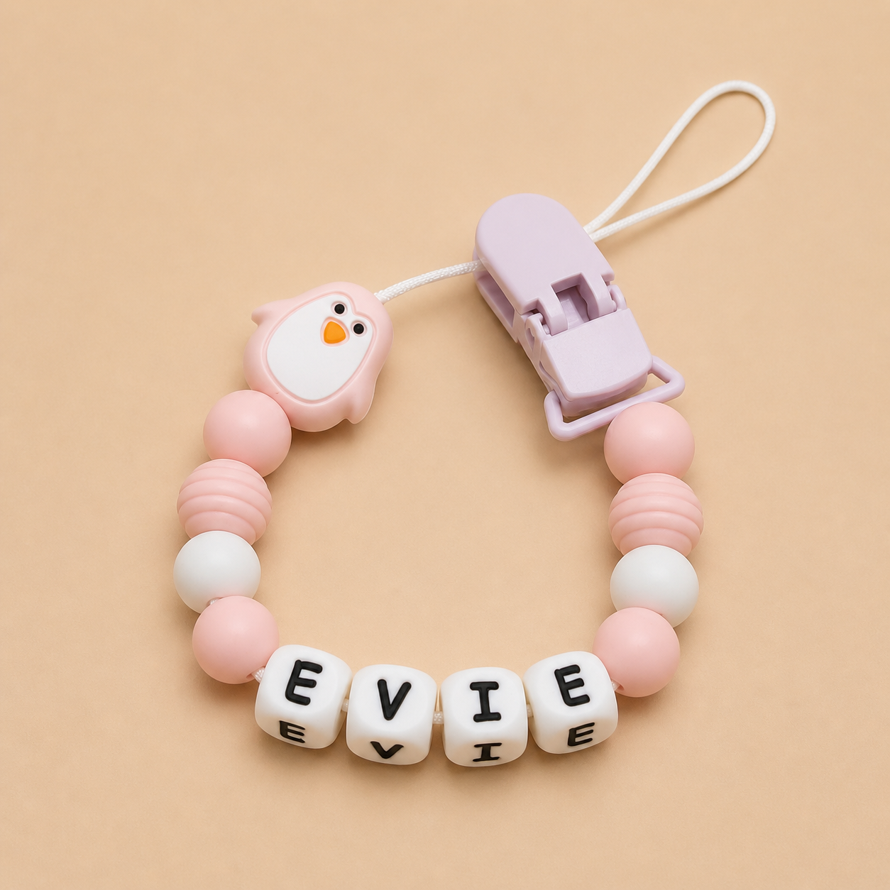 Baby dummy clip with pink beads and 'EVIE' letter blocks on a beige background