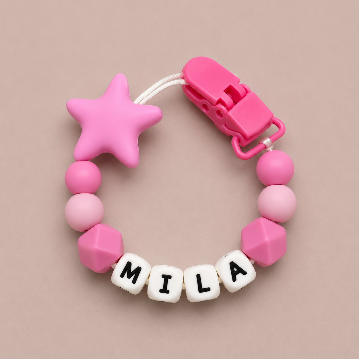 Pink baby dummy clip with star-shaped end and 'MILA' name beads on a beige background