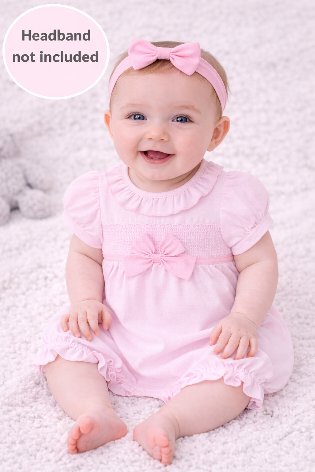 Baby in a pink outfit with a headband on a soft surface