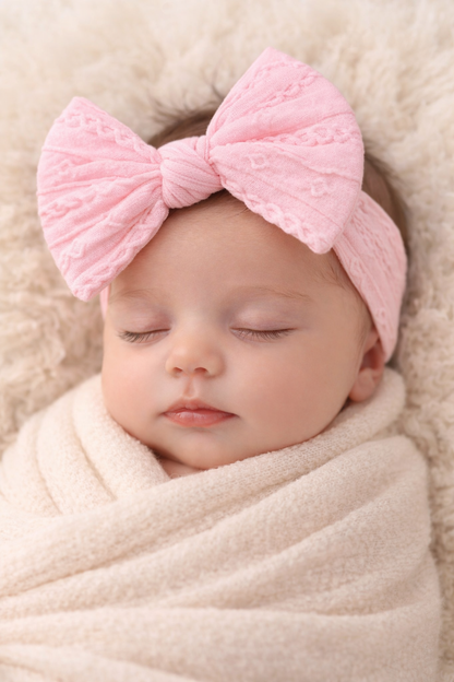 Newborn baby wrapped in a soft blanket with a pink knotted headband.