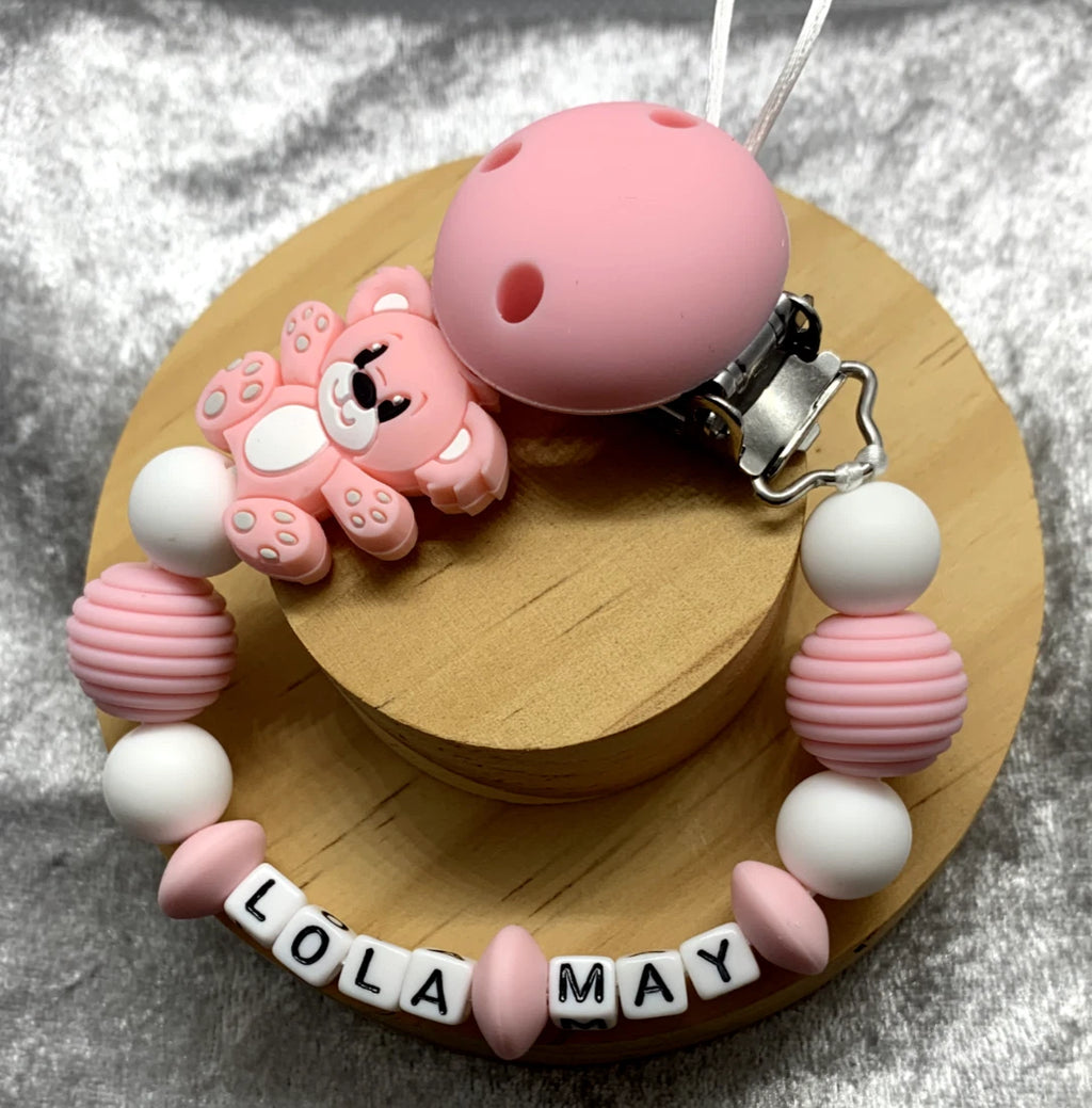 Pink teddybear dummy clip on a grey textured surface. Personalised with the name 'Lola-May'. Change of name is available in the personalisation box. MAM Adapters are available too.