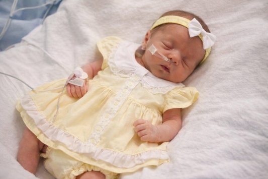 Newborn baby in a yellow dress with medical equipment on a white blanket