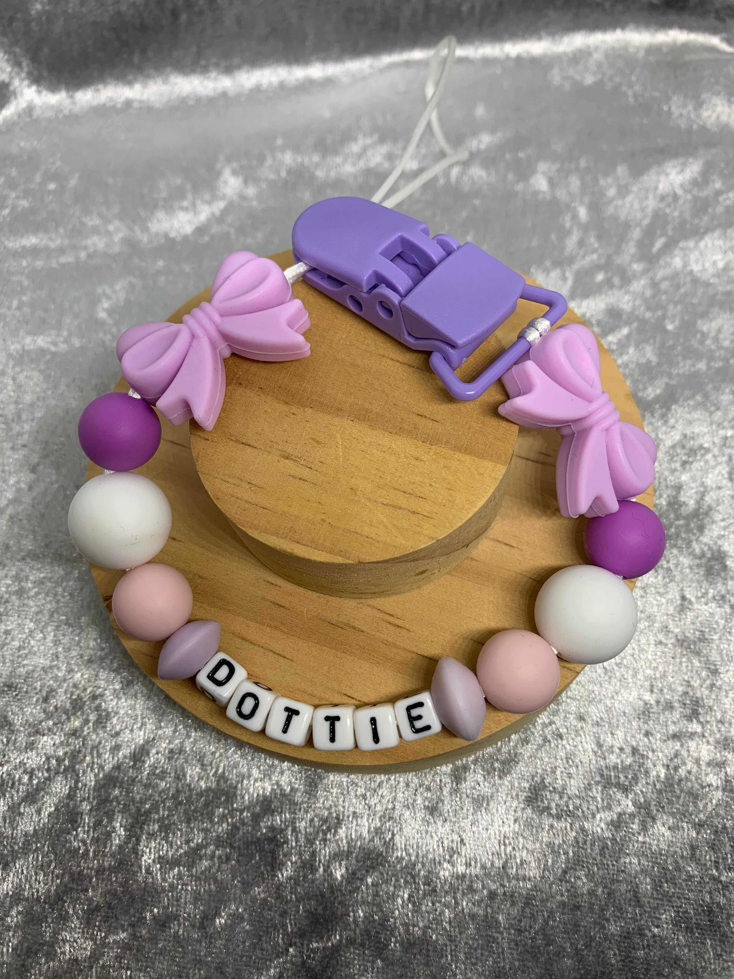 Pacifier clip with colorful beads and a purple clip on a textured gray background