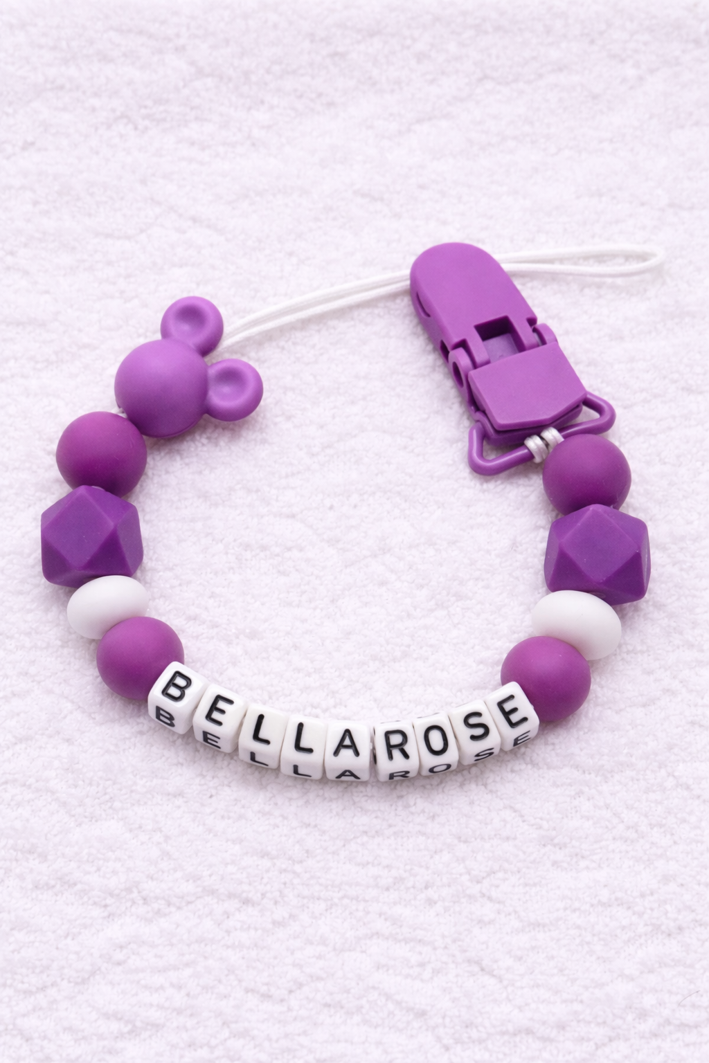 Purple and white baby dummy clip with 'BELLAROSE' branding on a textured white background