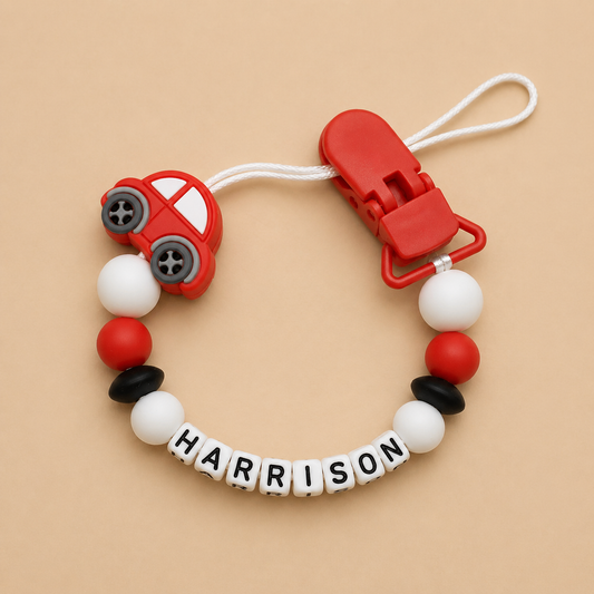 Baby dummy clip with red car design and 'HARRISON' name on a beige background