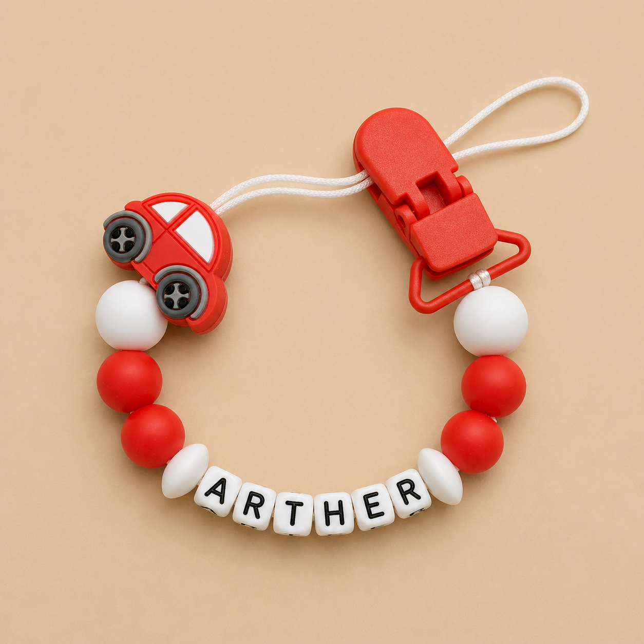 Red car-shaped clip with 'ARTHUR' on beads against a beige background