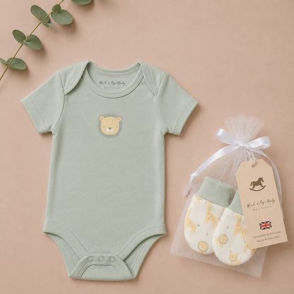 Green baby onesie with bear design and white mittens in clear bag on beige background