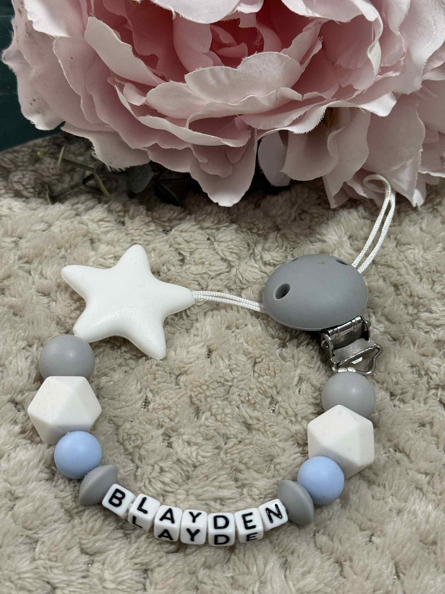 Blue, Grey And white silicone dummy clip on a beige textured surface. Personalisation options available