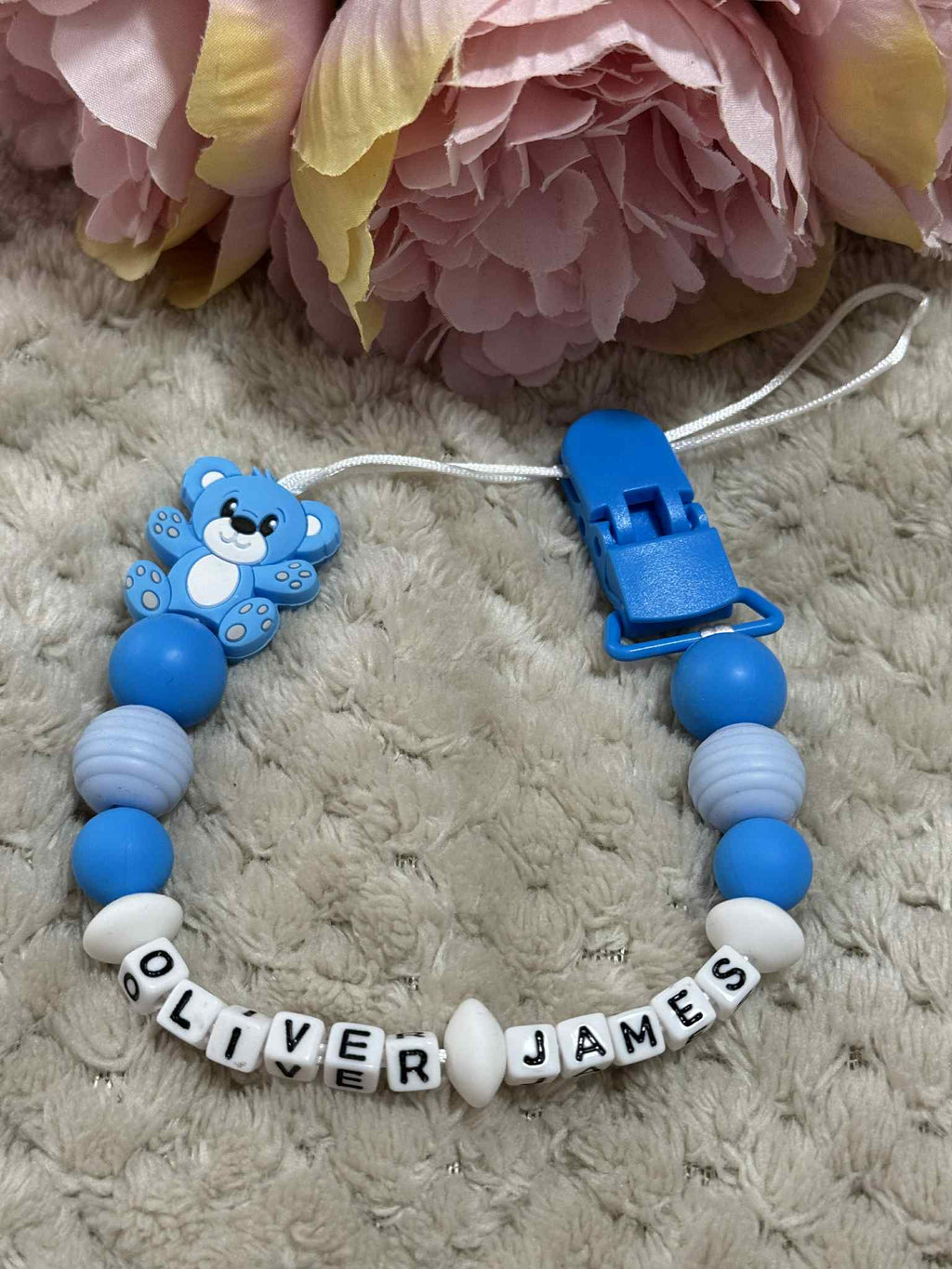 Blue and white teddybear dummy chain on a beige textured surface personalised with the name ''Oliver-James'. Personalisation and MAM Adapter options available.