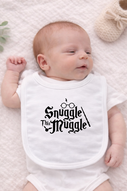 White baby bib displayed on a neutral fabric background featuring the phrase “Snuggle This Muggle” in a playful magical-style font, perfect for Harry Potter–inspired baby gifts.