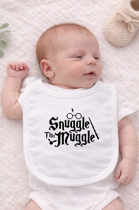 White baby bib displayed on a neutral fabric background featuring the phrase “Snuggle This Muggle” in a playful magical-style font, perfect for Harry Potter–inspired baby gifts.