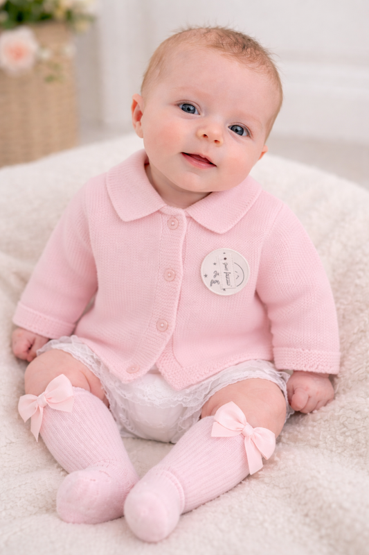 Baby wearing a pink cardigan on a white blanket