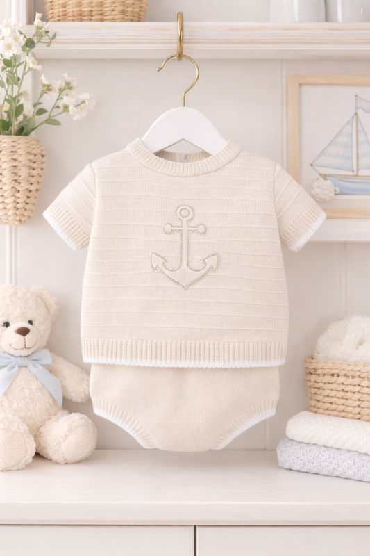 Beige baby romper with anchor design on a hanger against a white wall with decorative items.