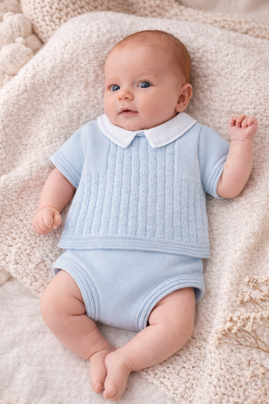 Baby wearing a light blue outfit with a white collar on a soft beige blanket.