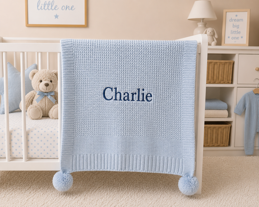 Blue baby blanket with 'Charlie' embroidered on it in a nursery setting.