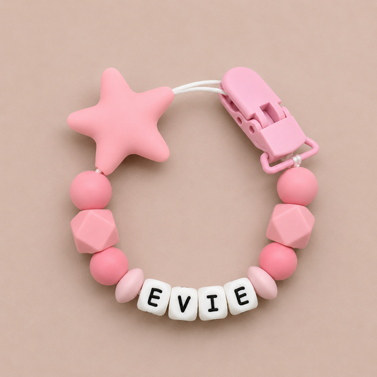 Pink baby dummy clip with geometric beads and a star-shaped clip on a beige background