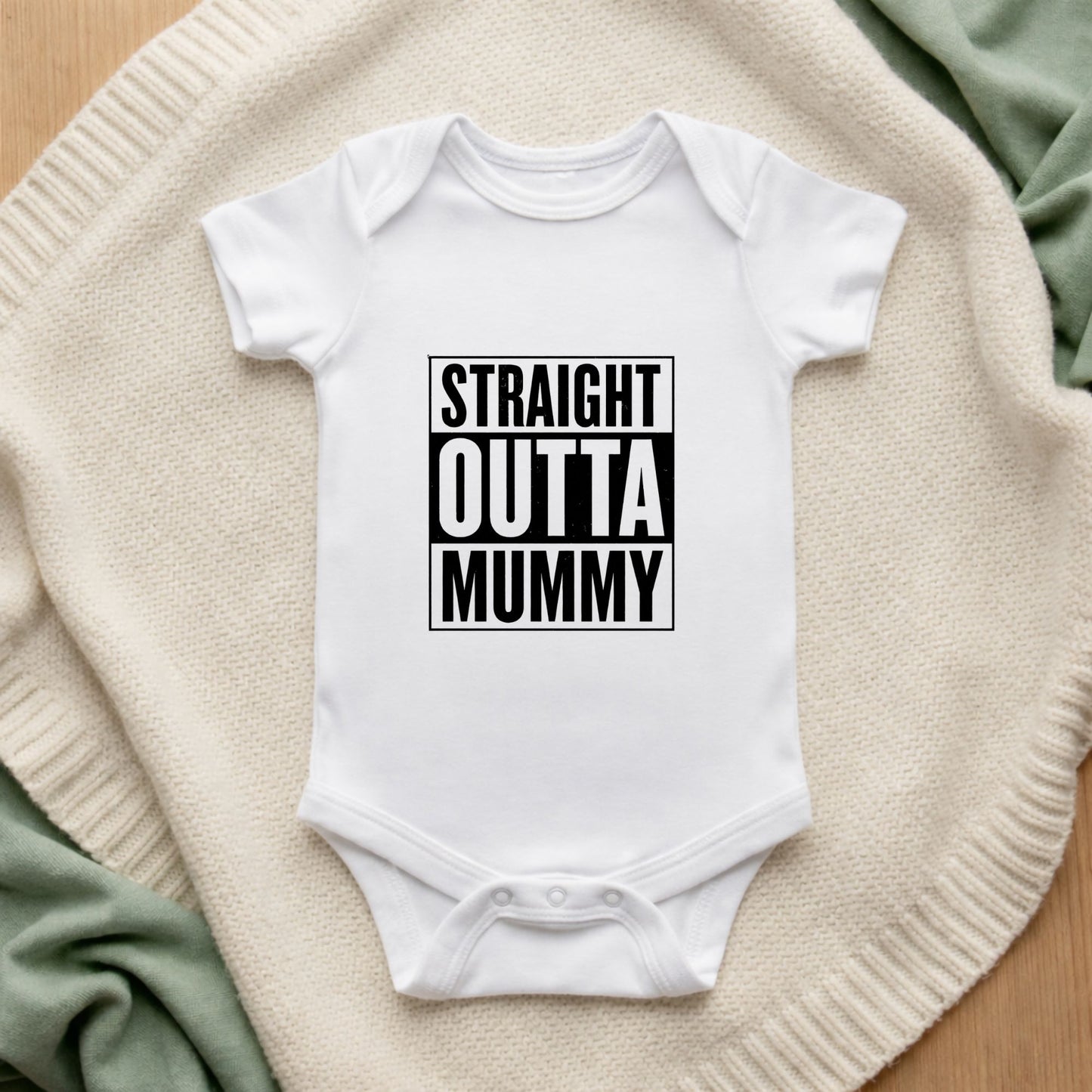 White baby onesie with 'STRAIGHT OUTTA MUMMY' text on a textured surface.