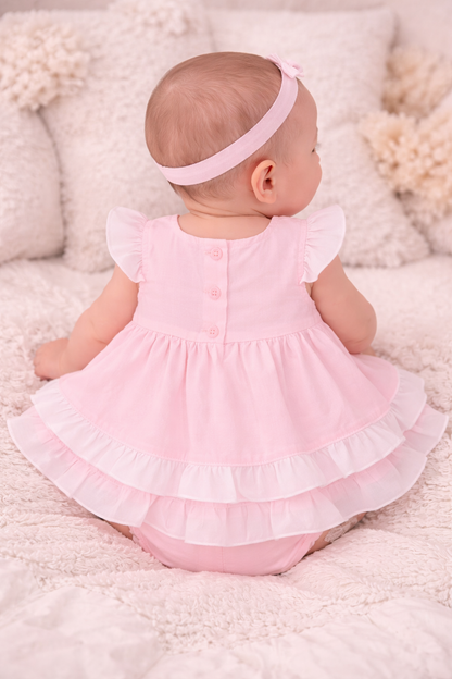 Baby in a pink dress sitting on a soft surface