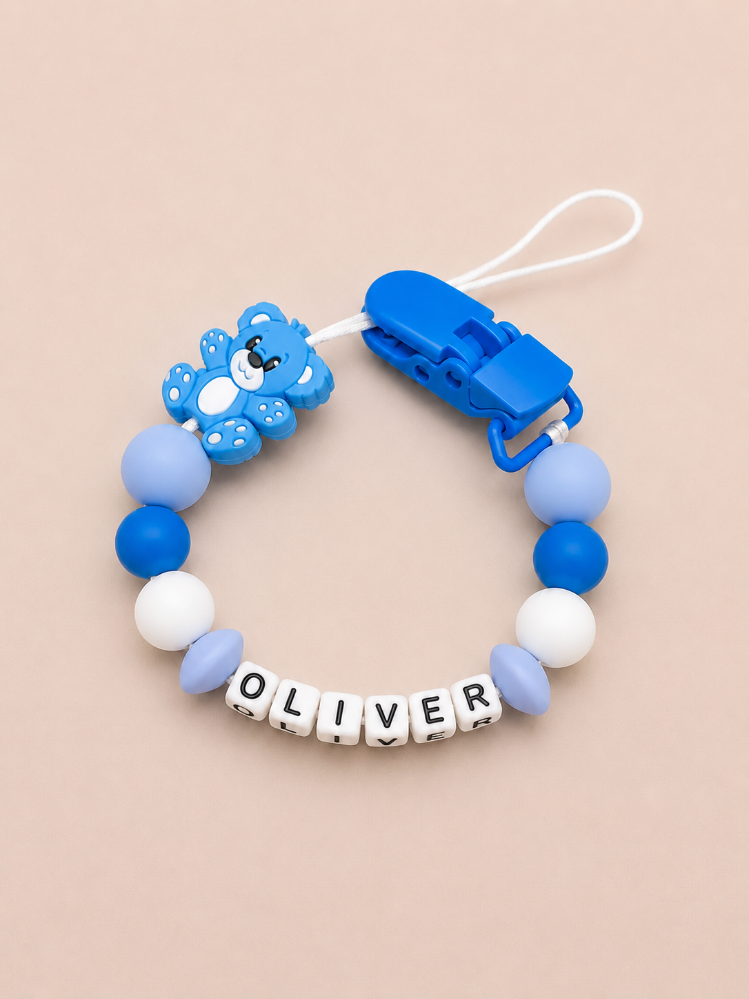 Blue and white dummy clip with 'OLIVER' on a beige background