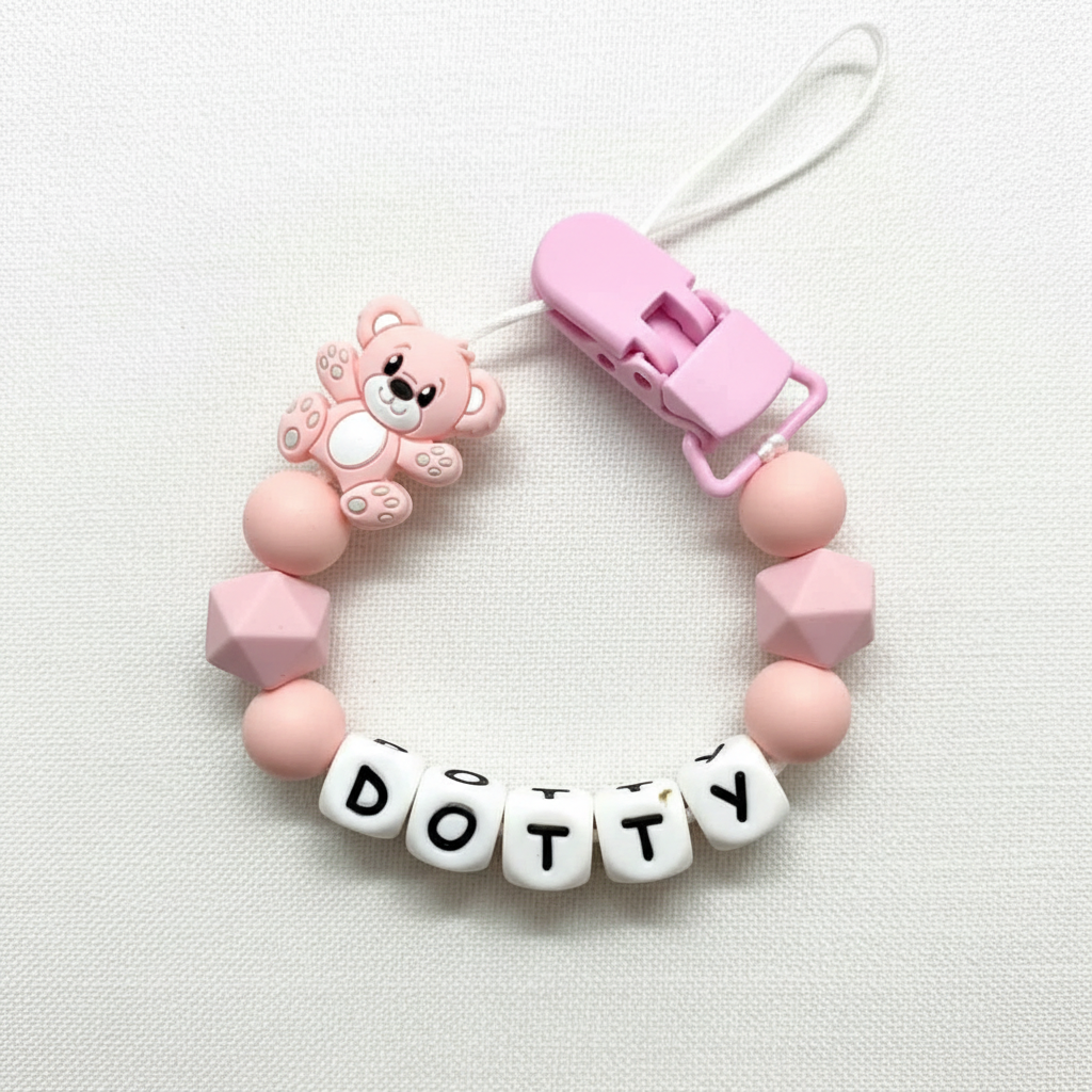 Personalised pink and peach teddy bear dummy clip on a soft white luxury linen textured background.