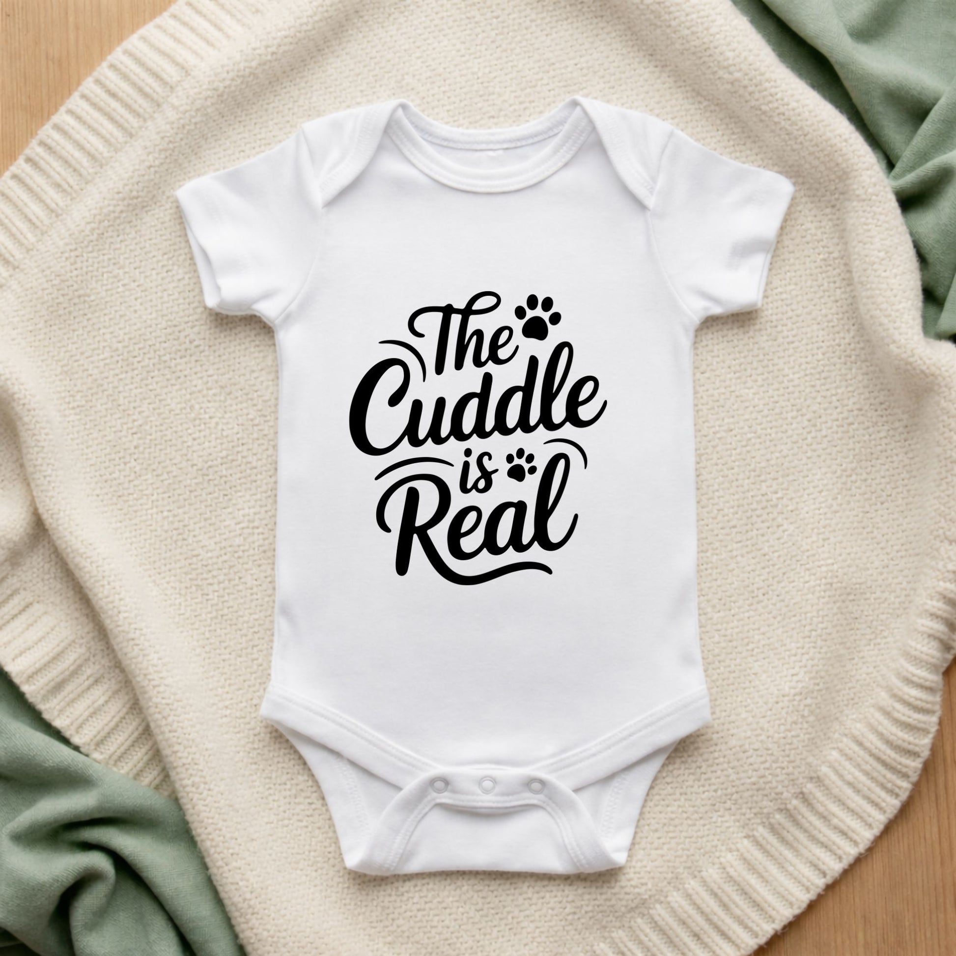 White baby onesie with 'The Cuddle is Real' text on a textured surface