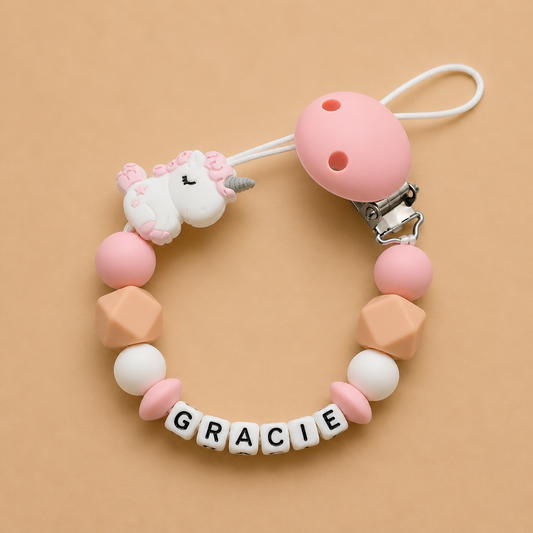 Pink and beige dummy clip with a unicorn charm and 'GRACIE' beads on a beige background