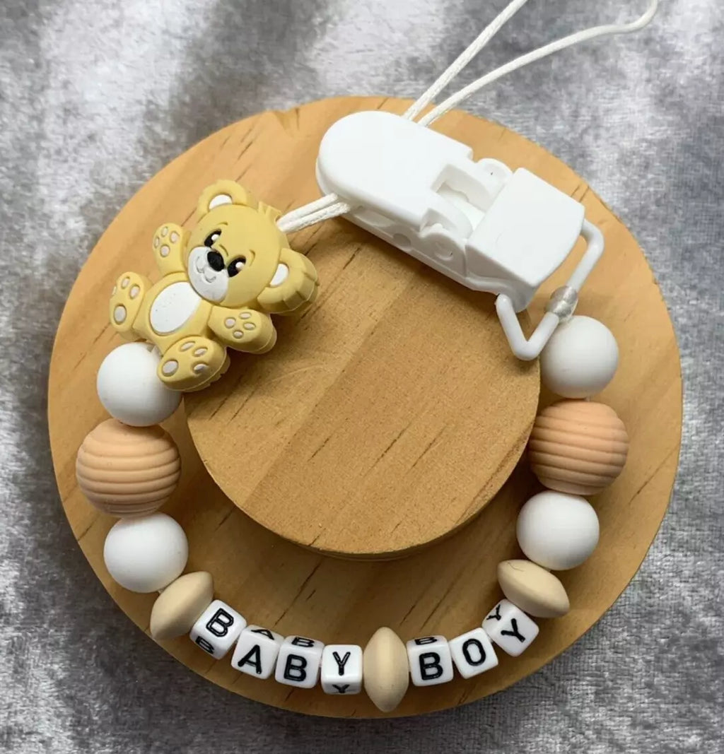 Cream and White teddybear dummy clip on a grey textured surface. Personalised with the name 'Baby Boy'. Change of name is available in the personalisation box. MAM Adapters are available too.