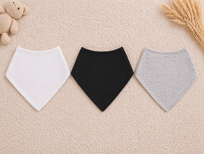 Three baby bibs in white, black, and gray on a beige surface.